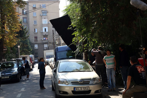  În stânga, regizorul Valentin Hotea îi dă ultimele indicaţii lui Şerban Pavlu, aflat la volan. În capătul străzii, un asistent se asigură că nicio altă maşină nu intră în cadru. 